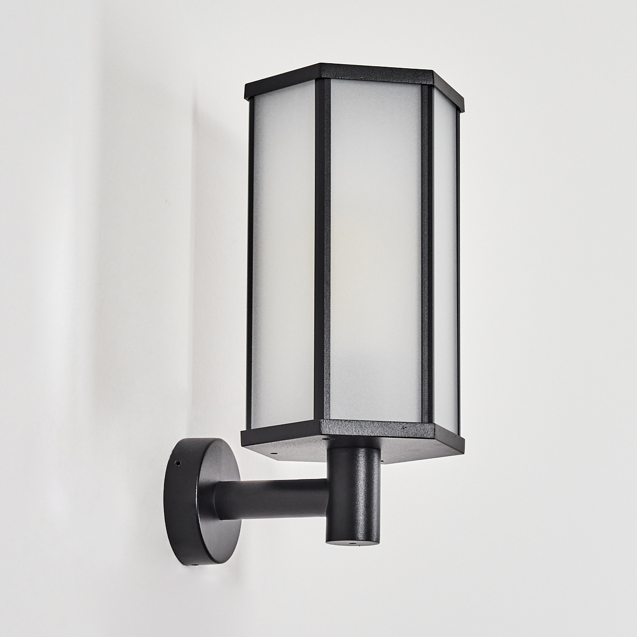 Schwarze Wandlampe mit rechteckigem, mattiertem Glasschirm. Die Lampe ist an einer weißen Wand befestigt. Der Schirm hat einen schwarzen Rahmen.