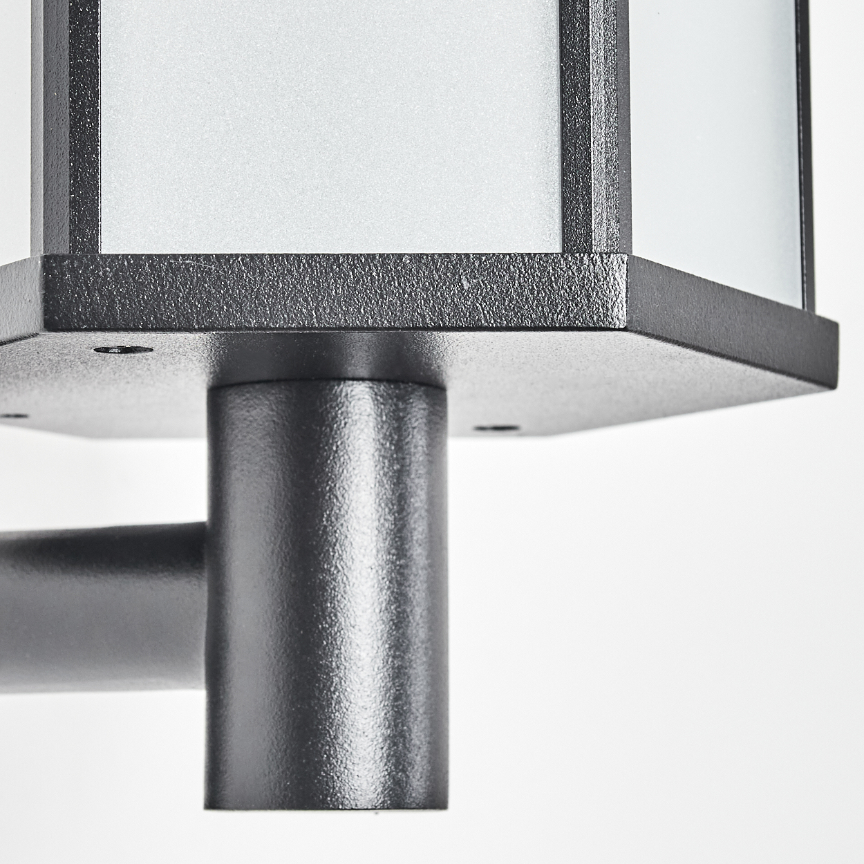 Nahaufnahme einer schwarzen Metalllampe. Sie hat einen quadratischen Sockel und einen zylindrischen Pfosten. Die Lampe hat einen weißen, mattierten Glasschirm.