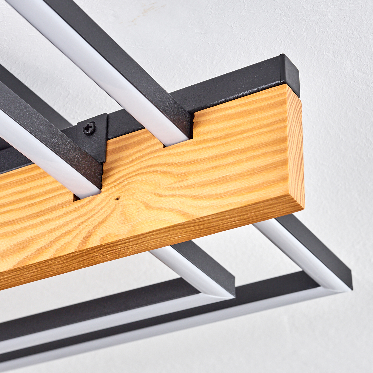 Nahaufnahme einer modernen Leuchte. Sie hat einen Holzbalken, Metallrahmen und helle weiße LED-Leuchten vor einer weißen Wand.