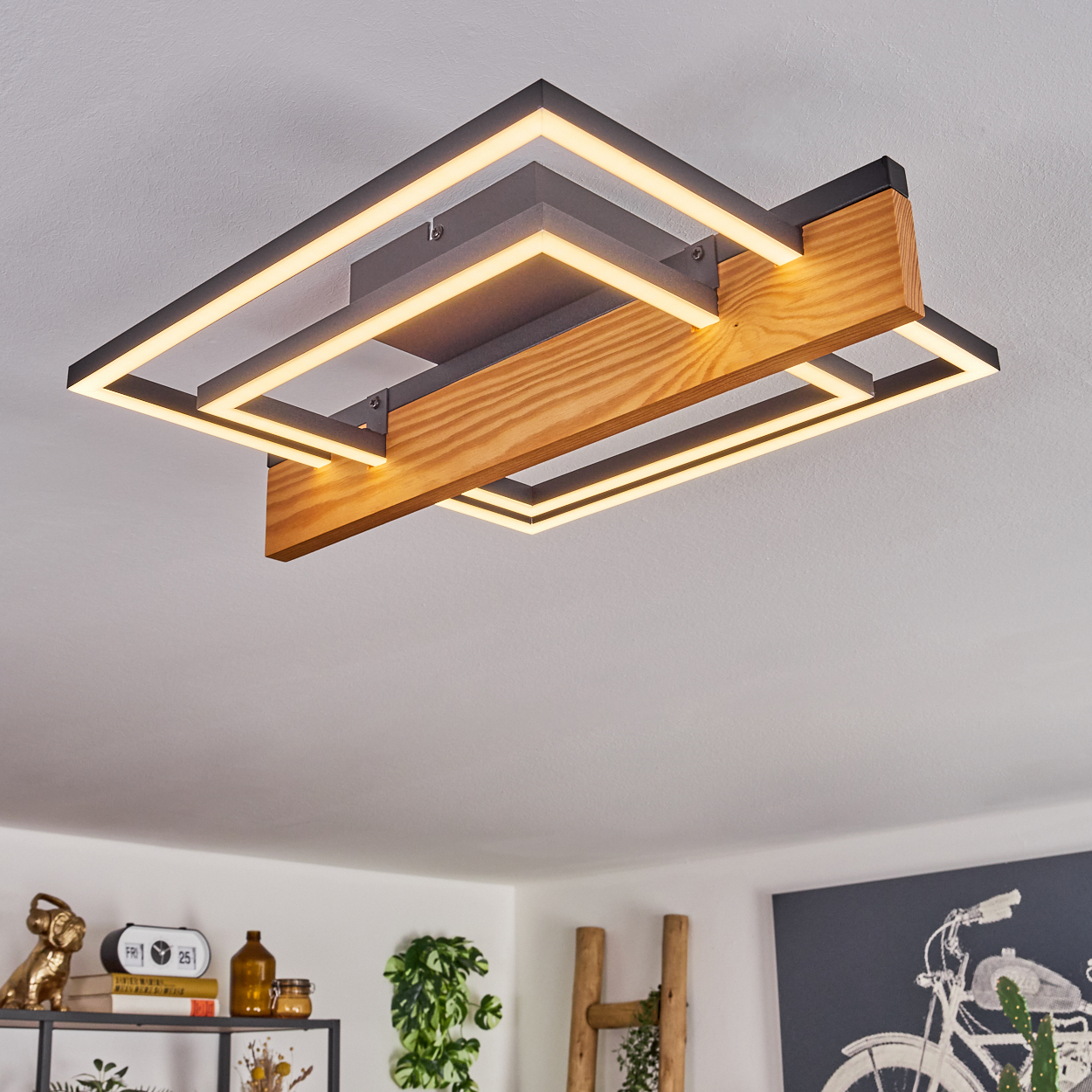 Eine moderne Deckenleuchte mit Holz- und Metallrahmen. Das Licht ist an. Andere Objekte im Raum sind im Hintergrund sichtbar.