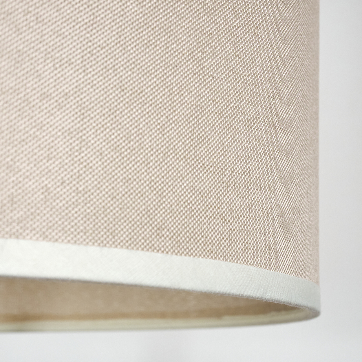 Nahaufnahme eines Lampenschirms. Der Lampenschirm ist beige mit gewebter Textur. Unten ist ein weißer Rand und ein weißer Hintergrund.