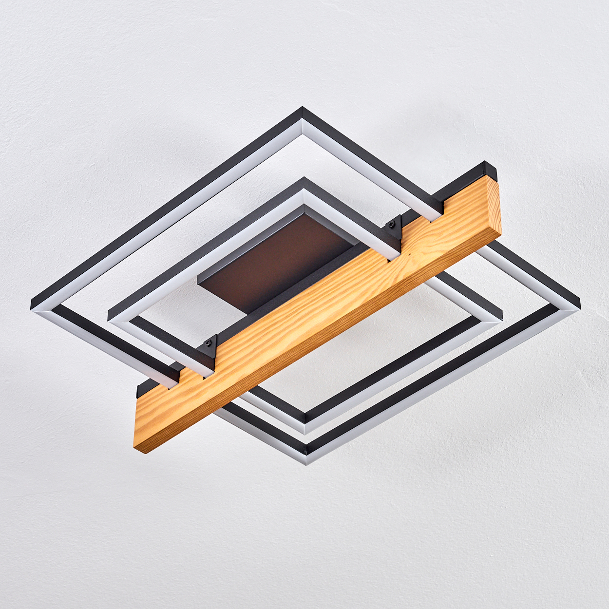 Eine Deckenleuchte mit schwarzen quadratischen Rahmen, weißen Lichtern, einem Holzbalken und einem schwarzen rechteckigen Zentrum vor weißer Decke.