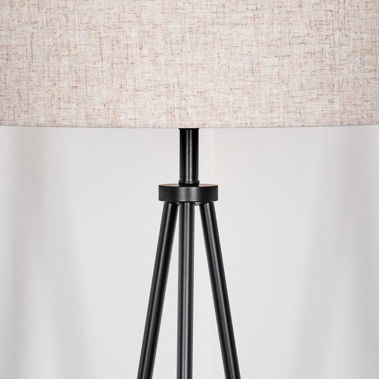 Eine schwarze Stativlampe mit beigefarbenem Lampenschirm. Der Hintergrund ist eine schlichte weiße Wand. Die Lampe ist zentriert.