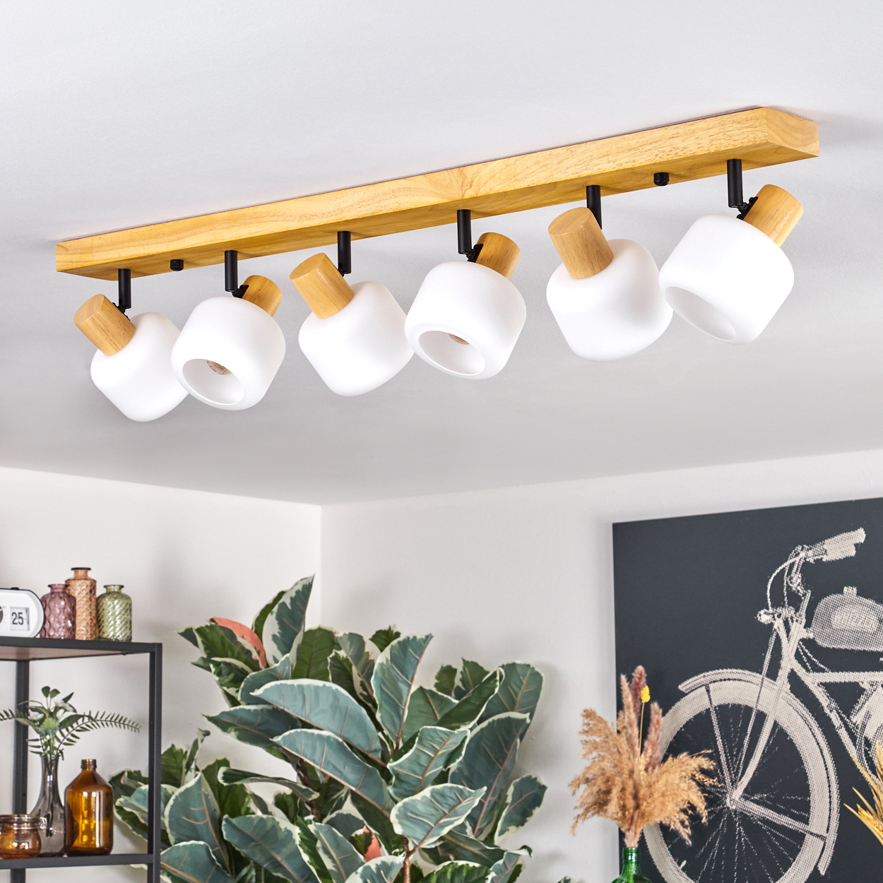 Deckenleuchte mit sechs weißen Lampen. Holzbalken und Holzakzente. Pflanzen und ein Fahrradkunstwerk im Hintergrund.