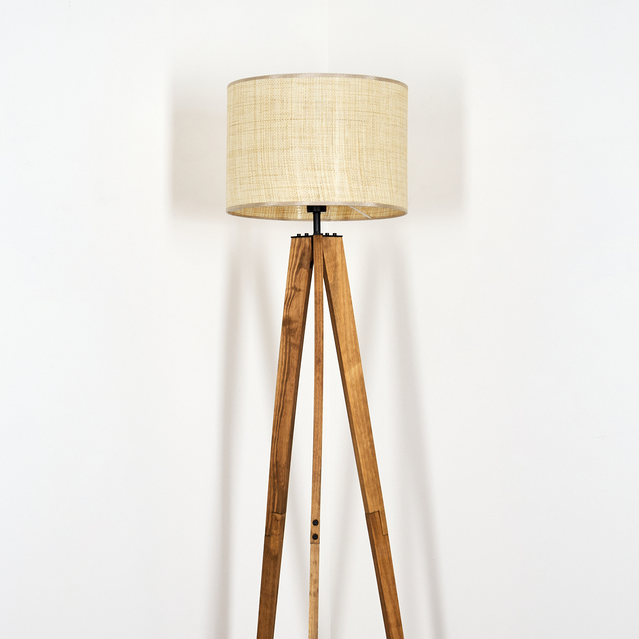 Eine Holz-Stativ-Stehlampe mit beigem Lampenschirm steht vor einer weißen Wand. Die Lampe hat eine natürliche Holzoberfläche.