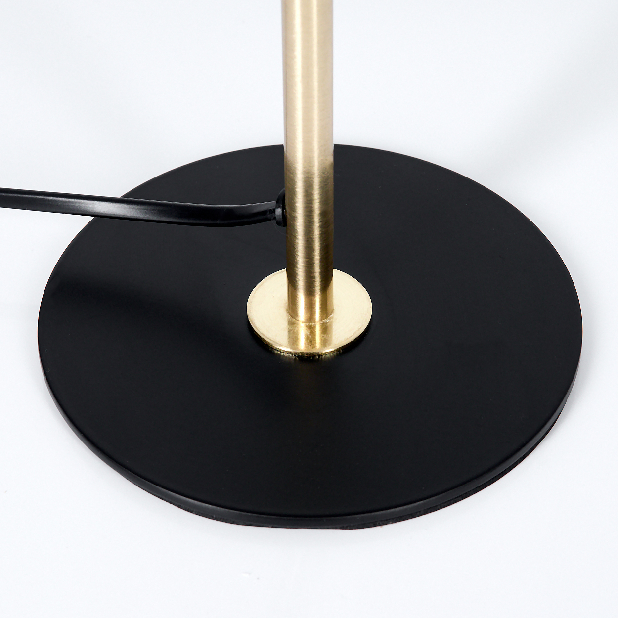 Nahaufnahme zeigt schwarzen, kreisförmigen Lampenfuß. Eine goldfarbene Stange ragt aus der Mitte, mit einem schwarzen Kabel.
