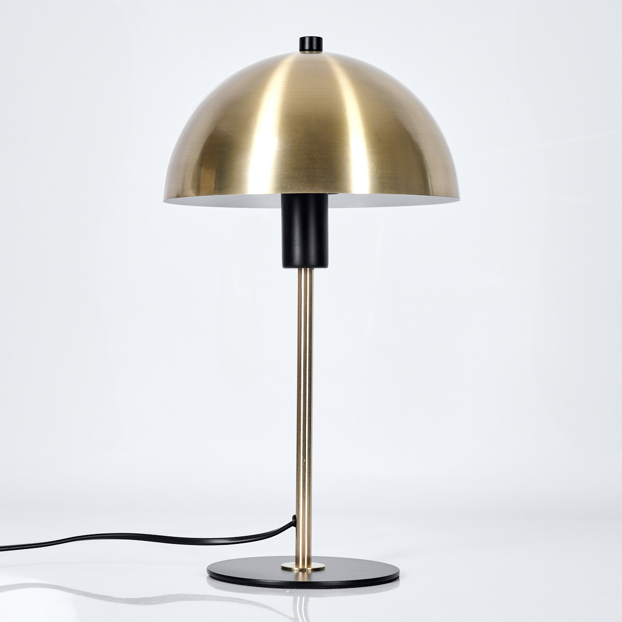 Eine moderne Tischlampe mit goldfarbenem Kuppel-Schirm, schwarzem Stiel und Fuß sowie einem schwarzen Netzkabel auf weißem Hintergrund.