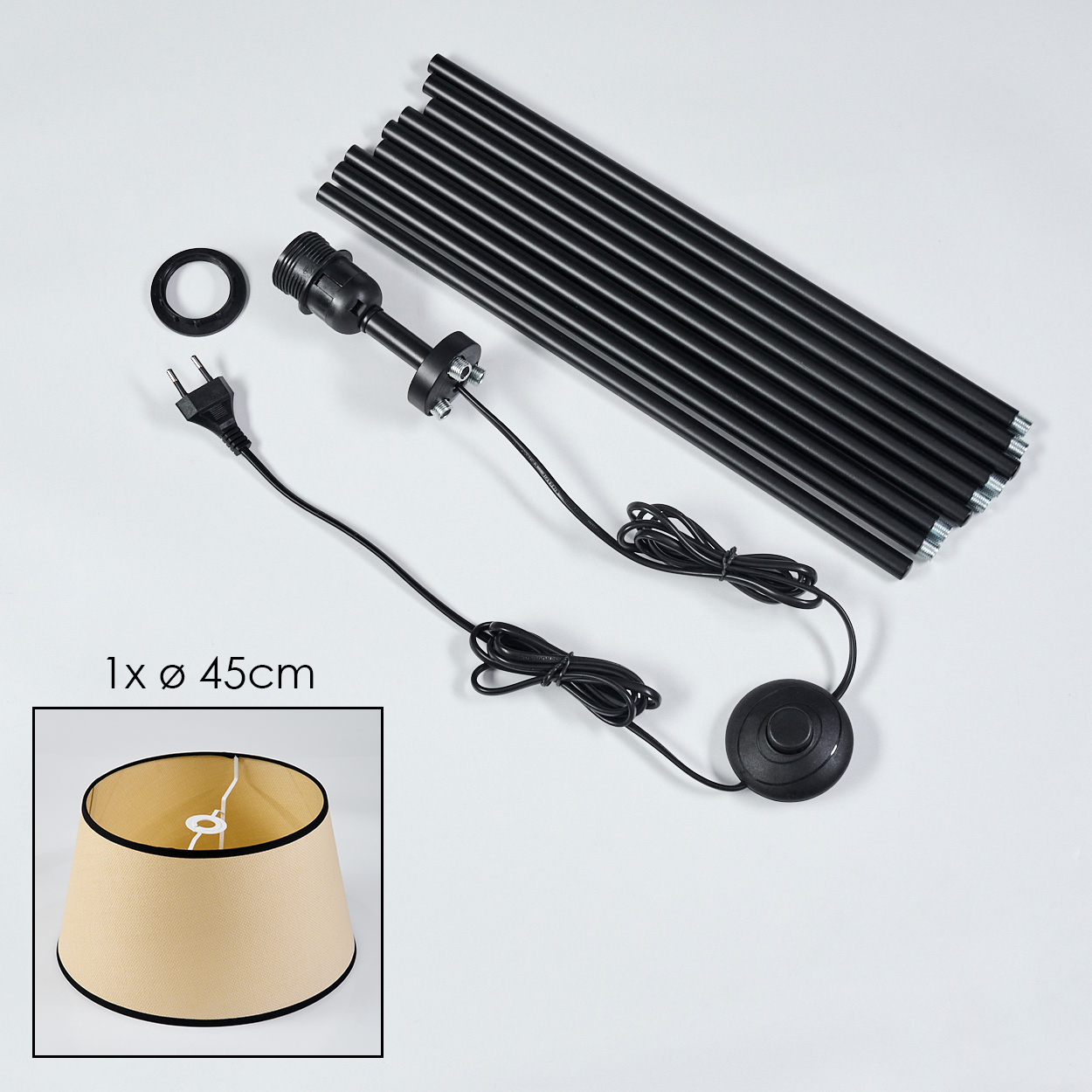 Zerlegte Lampenteile: schwarze Stangen, Schirm, Fassung, Kabel und Schalter. Beigefarbener Lampenschirm mit schwarzem Rand. Komponenten auf weißer Fläche.