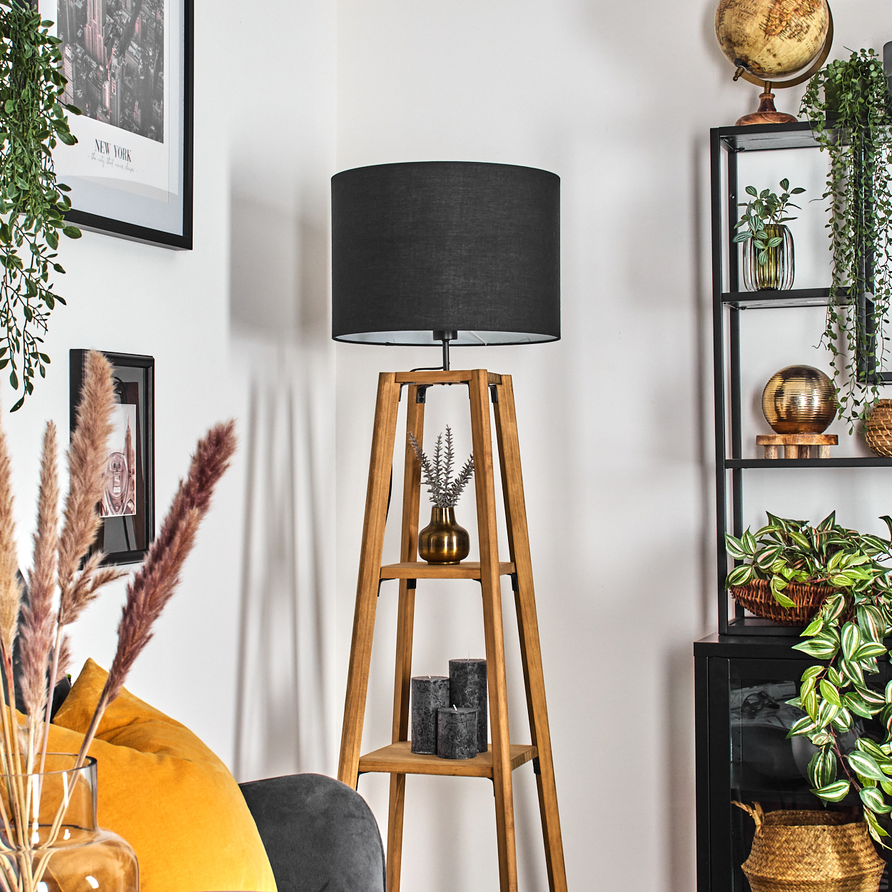 Eine Holzlampe mit schwarzem Lampenschirm. Ein Bücherregal mit Pflanzen und einem Globus. Eine Vase mit Blumen. Kerzen auf einem Regal.