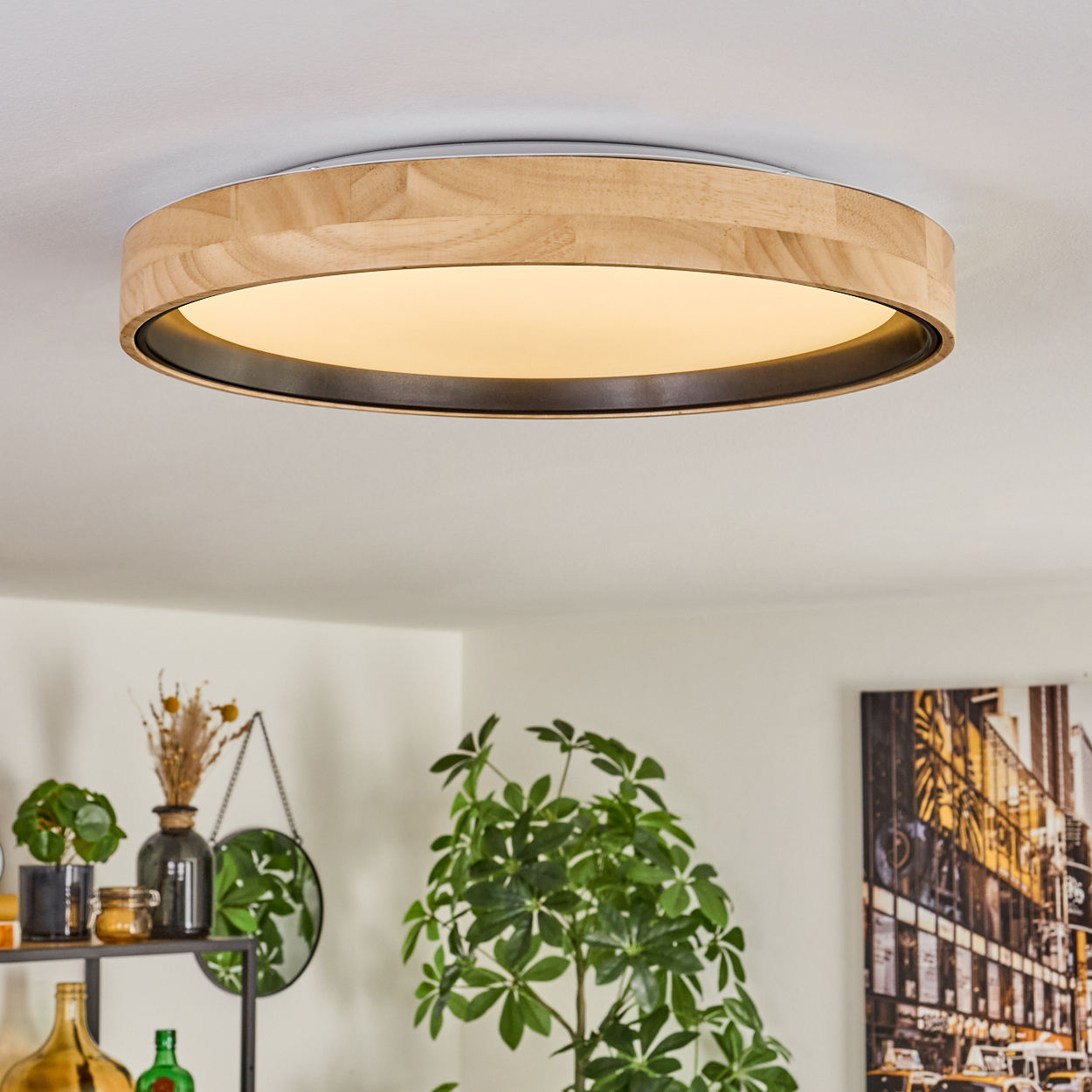 Eine Deckenleuchte aus Holz. Darunter Pflanzen und ein Spiegel. Im Hintergrund ein Bild einer Stadtszene. Das Licht ist an.