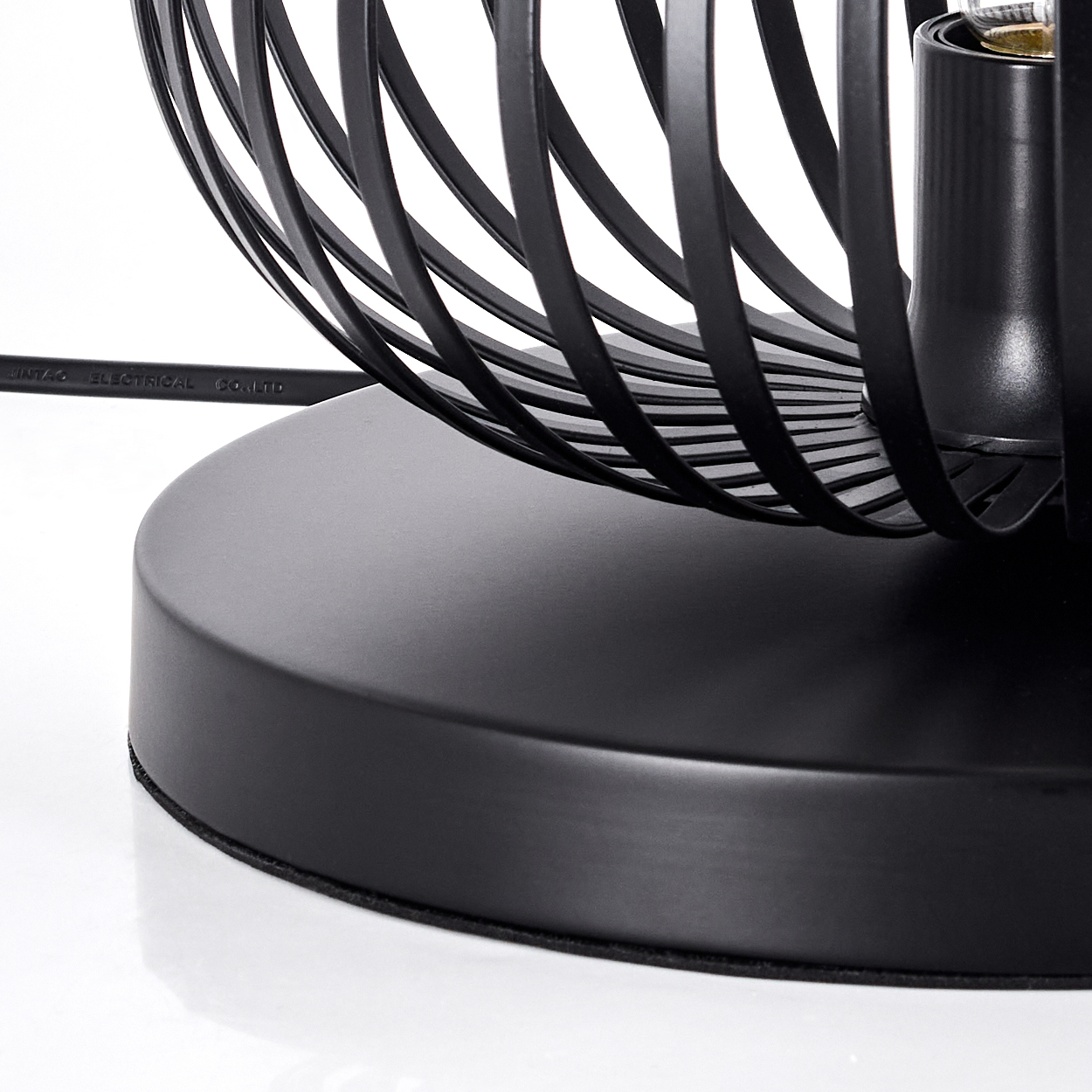 Schwarzer Lampenfuß mit Drahtkäfig-Design. Ein schwarzes Elektrokabel erstreckt sich vom Fuß. Der Hintergrund ist weiß.
