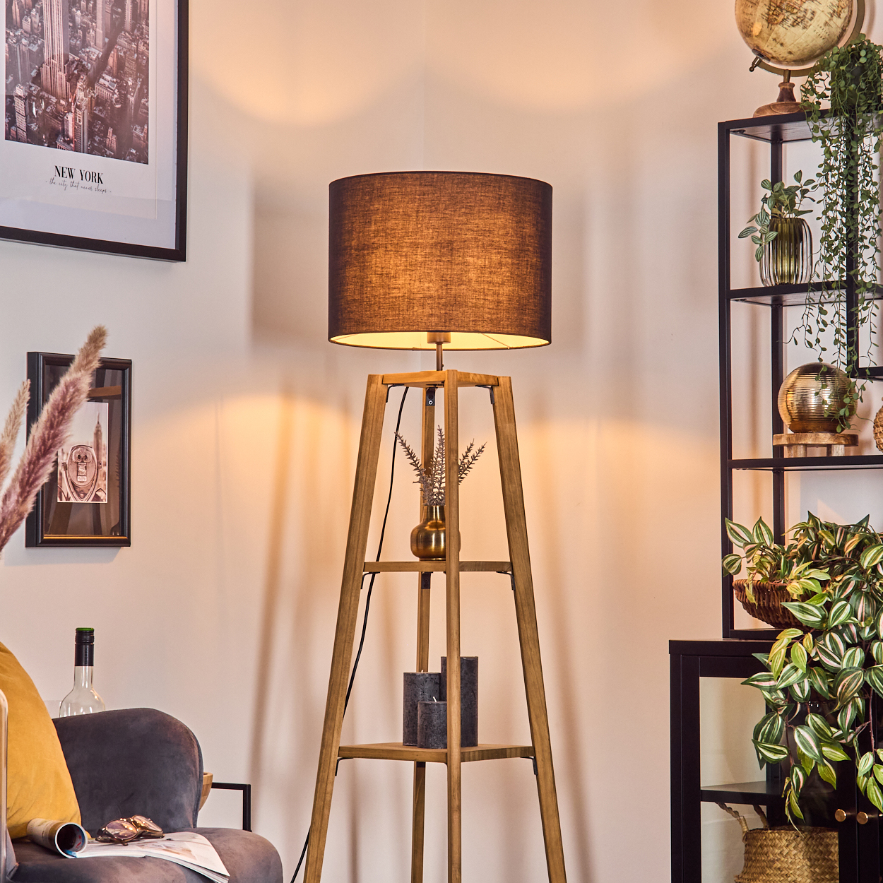 Eine hölzerne Stehlampe mit dunklem Schirm. Ein schwarzes Regal mit Pflanzen und einem Globus. Ein New York-Stadt-Druck an der Wand.