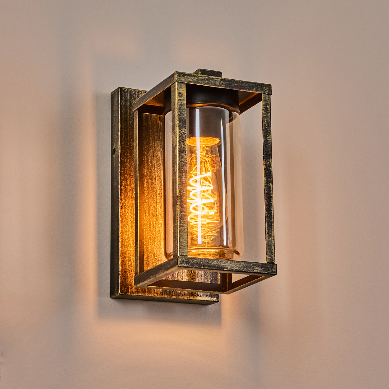 Eine Wandlampe mit rechteckigem Rahmen und Glaszylinder. Im Inneren ist eine glühende, spiralförmige Glühbirne zu sehen.