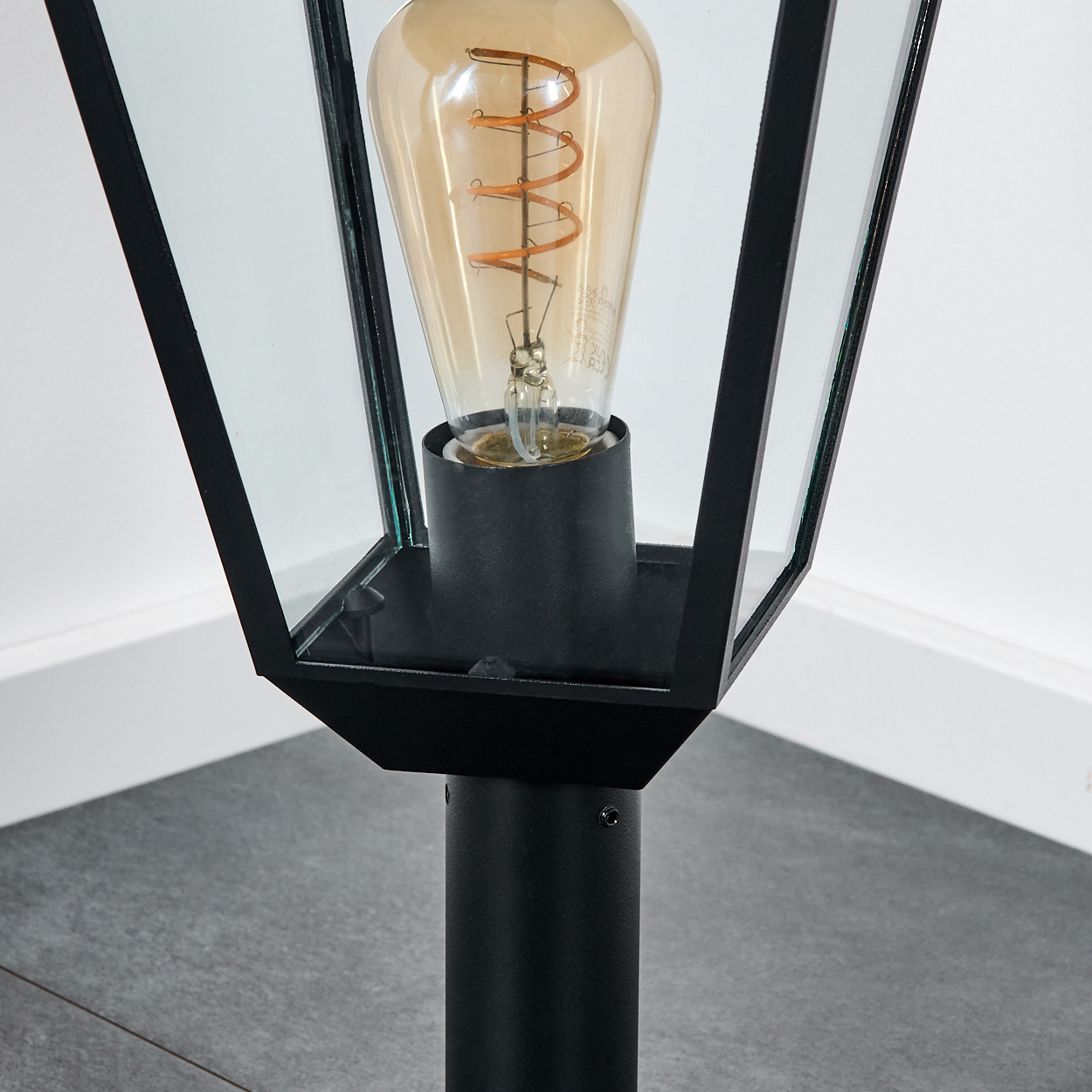 Eine schwarze Außenlampe mit Glasscheiben und einer großen Glühbirne mit Wendel. Der Hintergrund ist hell.