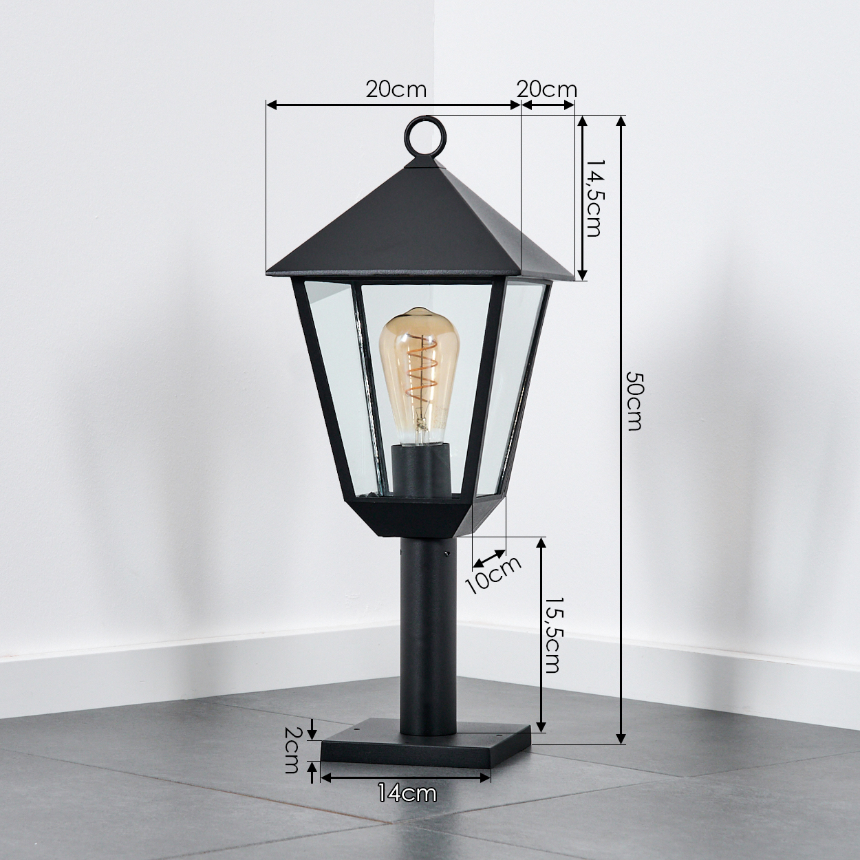 Schwarze Außenlampe mit Maßangaben. Sie hat eine Glühbirne, einen schwarzen Sockel auf Fliesenboden, vor weißer Wand.