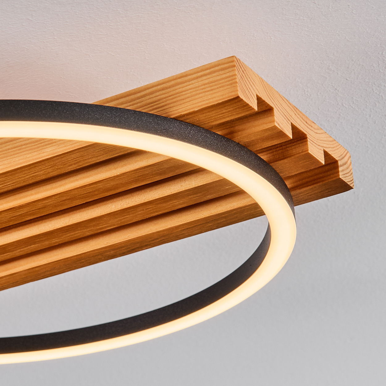 Eine moderne Leuchte mit einem kreisförmigen Leuchtring und einem Holzlatten-Design. Der Hintergrund ist eine schlichte weiße Decke.