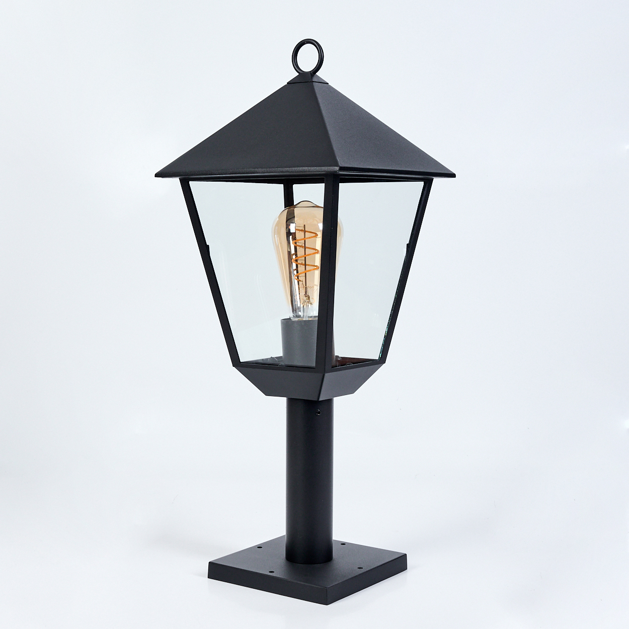 Schwarze Außenlampe auf weißem Hintergrund. Sie hat ein Glasgehäuse mit sichtbarer Glühbirne und einen Ring oben. Die Basis ist quadratisch.