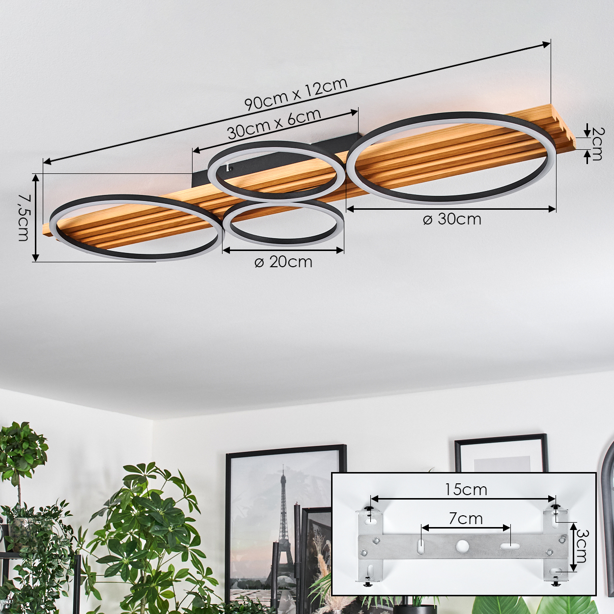 Moderne Deckenleuchte mit vier kreisförmigen Lichtern, Holzsockel und Maßangaben. Pflanzen und Kunstwerke im Hintergrund.