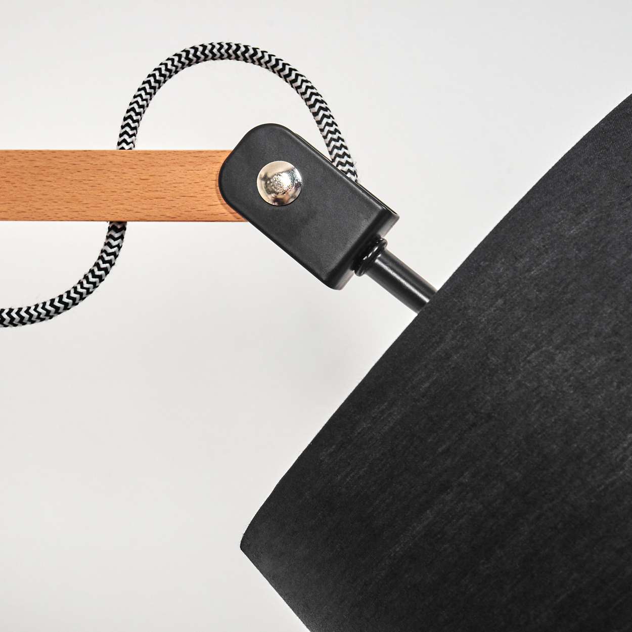 Nahaufnahme einer modernen Lampe. Sie hat einen schwarzen Lampenschirm, einen Holzarm und ein schwarz-weiß gemustertes Kabel auf weißem Hintergrund.