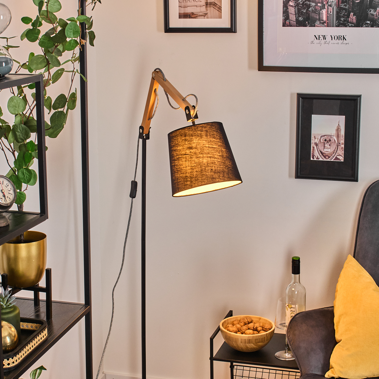 Ein schwarzer Lampenschirm auf einer Stehlampe aus Holz und schwarzem Metall. Bilder an der Wand, ein Stuhl und ein kleiner Tisch.