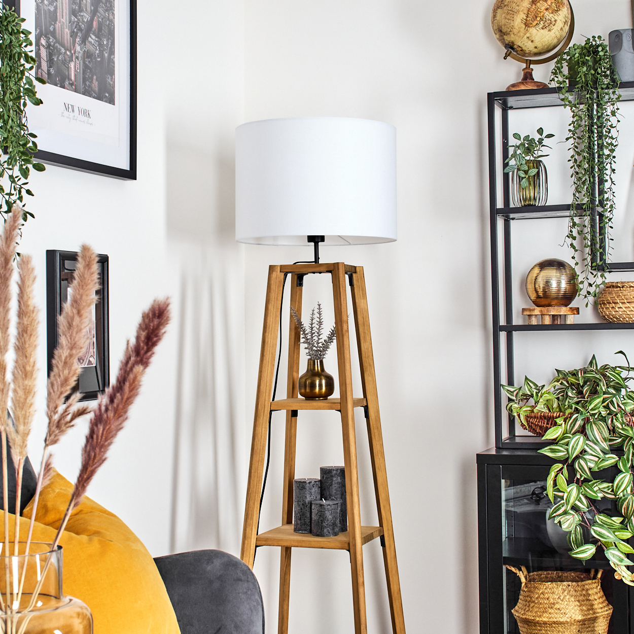 Eine Holzlampe mit weißem Lampenschirm steht neben einem Regal mit Dekor und Pflanzen. Ein Globus und Kunstwerk sind ebenfalls zu sehen.