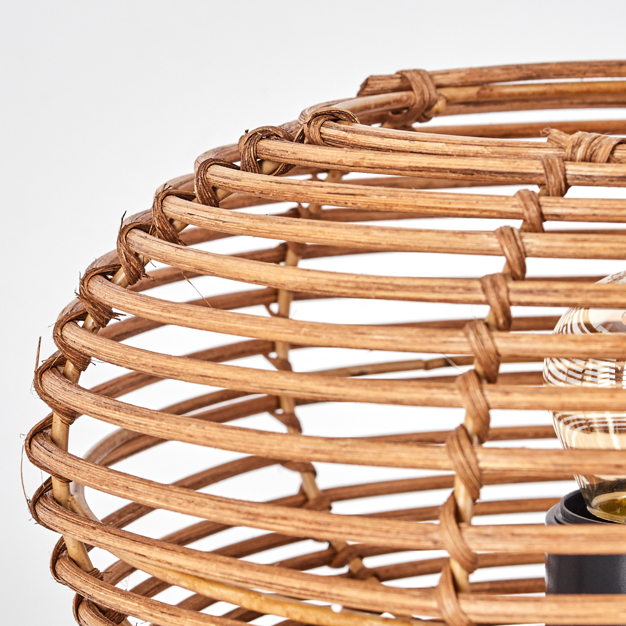 Nahaufnahme eines gewebten Lampenschirms aus Rattan. Der Schirm ist braun, mit einer sichtbaren Glühbirne. Der Hintergrund ist weiß.