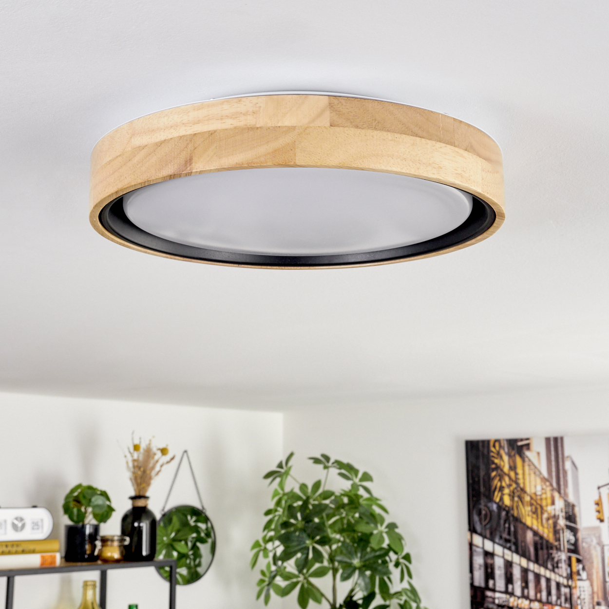 Eine Deckenleuchte mit Holzrahmen und weißem Diffusor ist an einer weißen Decke montiert. Darunter ein Raum mit Pflanzen und Dekoration.