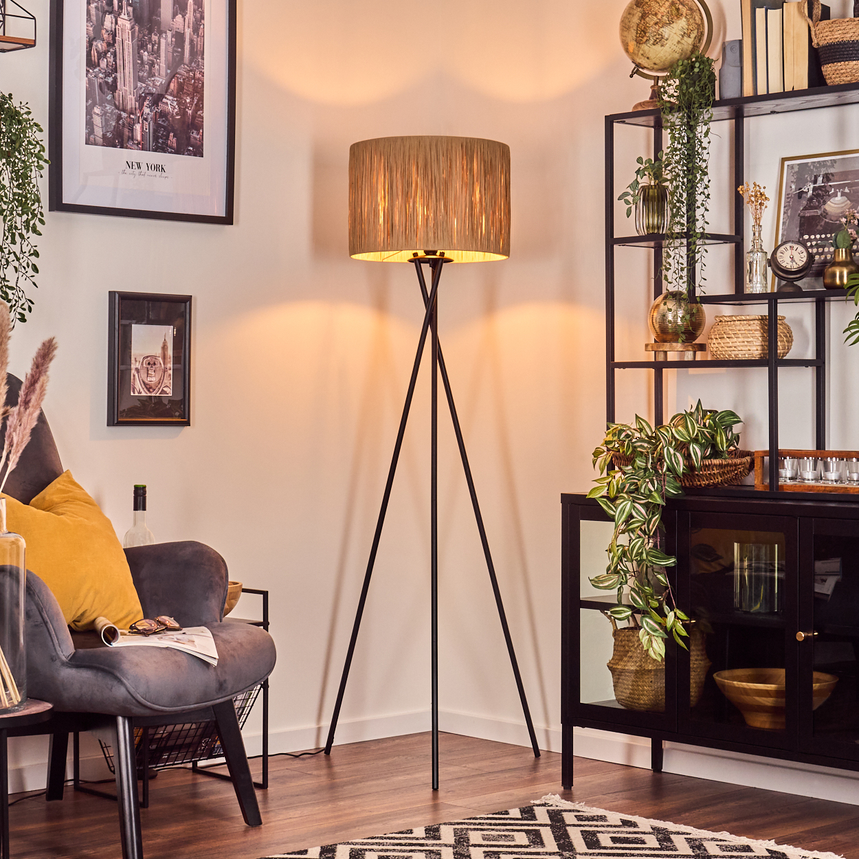 Ein Zimmer mit Stehlampe, Sessel und schwarzem Regal mit Dekoration. Ein New York-Poster hängt an der Wand. Auf dem Boden liegt ein Teppich.