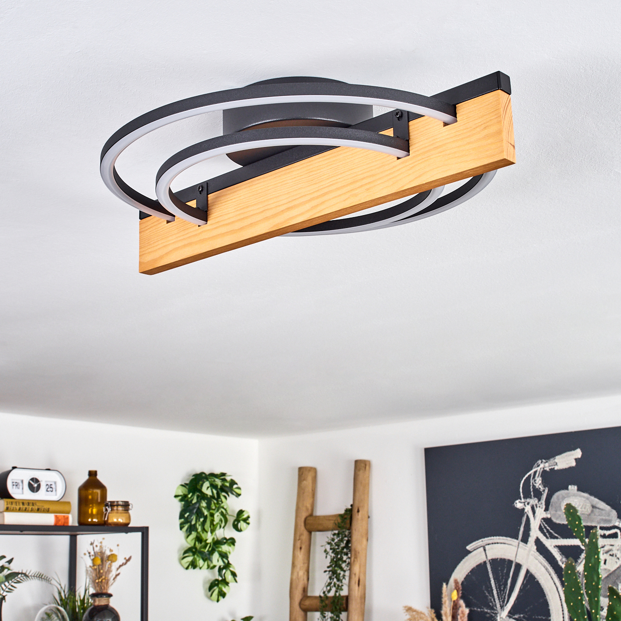 Eine Deckenleuchte mit Holzbalken und schwarzen Metallringen. Im Hintergrund Dekoration und ein Fahrradkunstwerk.