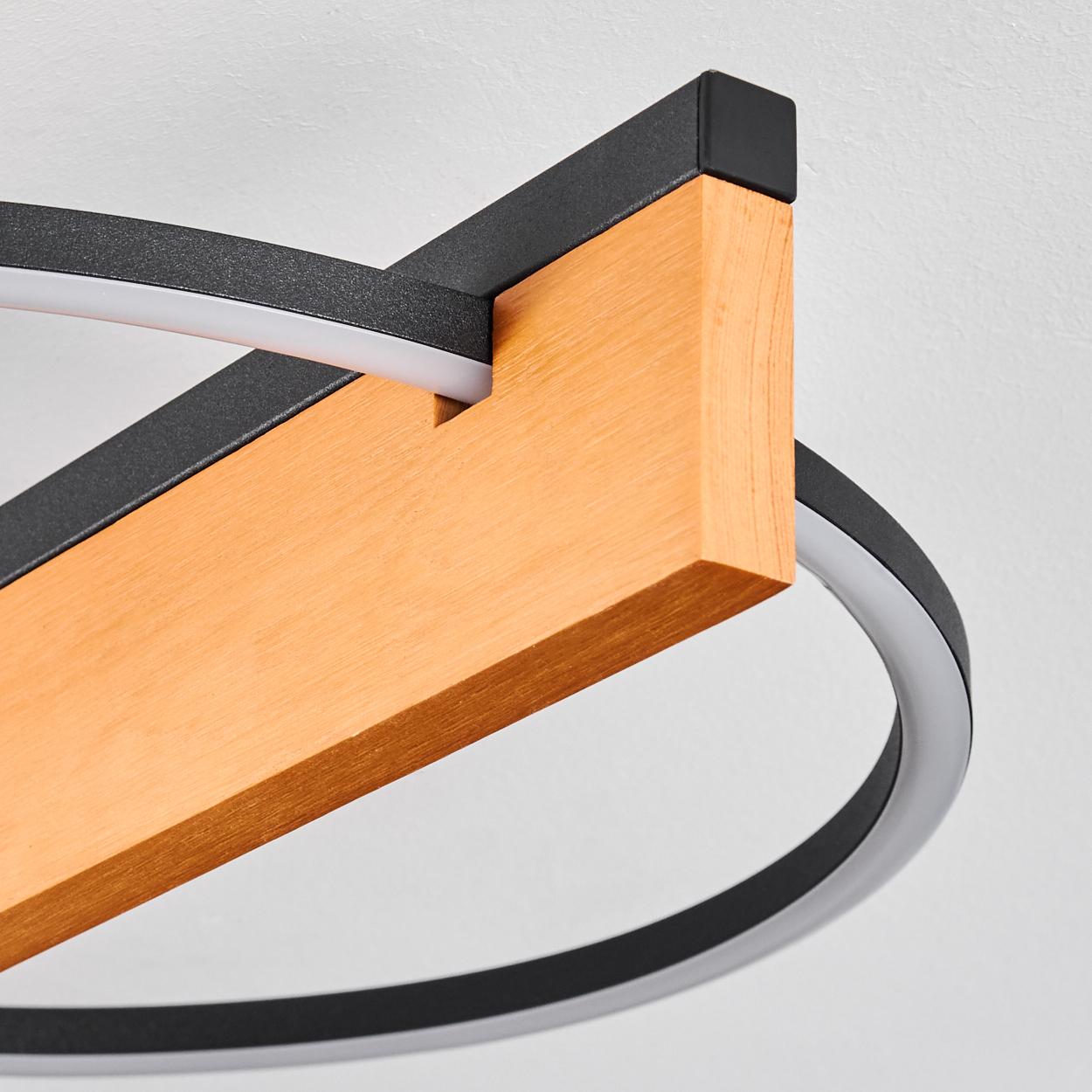 Moderne Deckenleuchte mit Holzbalken, schwarzen Metallakzenten und weißem, kreisförmigem LED-Licht. Der Hintergrund ist schlicht weiß.