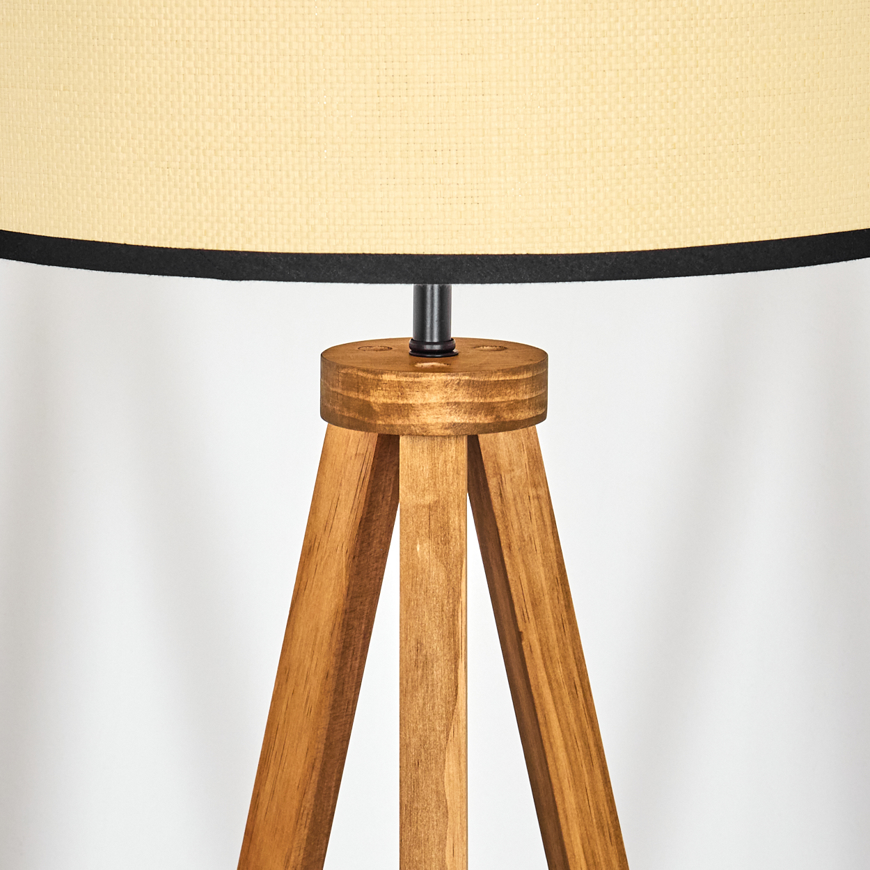 Nahaufnahme einer Holz-Stativlampe. Beigefarbener Lampenschirm mit schwarzem Rand. Holzbeine und eine runde Holzbasis stützen den Lampenschirm.