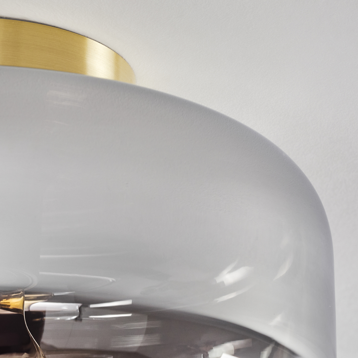 Nahaufnahme einer modernen Lampe. Ein messingfarbener Deckel und ein großer, abgerundeter, gräulich-weißer Schirm sind zu sehen.