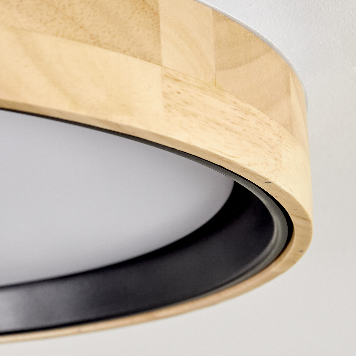 Nahaufnahme einer modernen Deckenlampe. Sie hat einen Holzrahmen, einen schwarzen Rand und eine weiße, leuchtende Oberfläche.