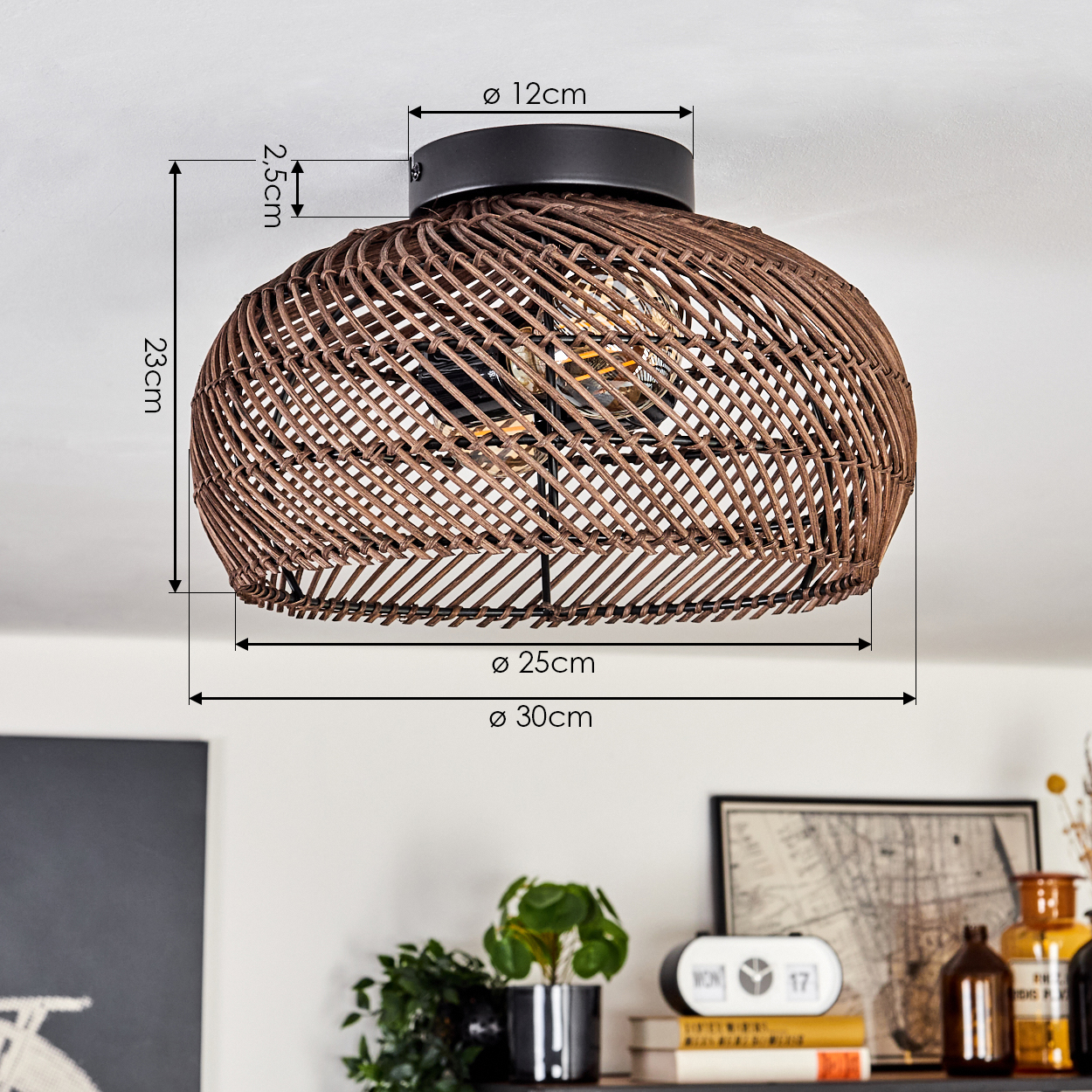 Eine braune Deckenlampe aus geflochtenem Rattan mit Maßangaben. Darunter ein Regal mit Pflanzen, einer Uhr, Büchern und dekorativen Flaschen.