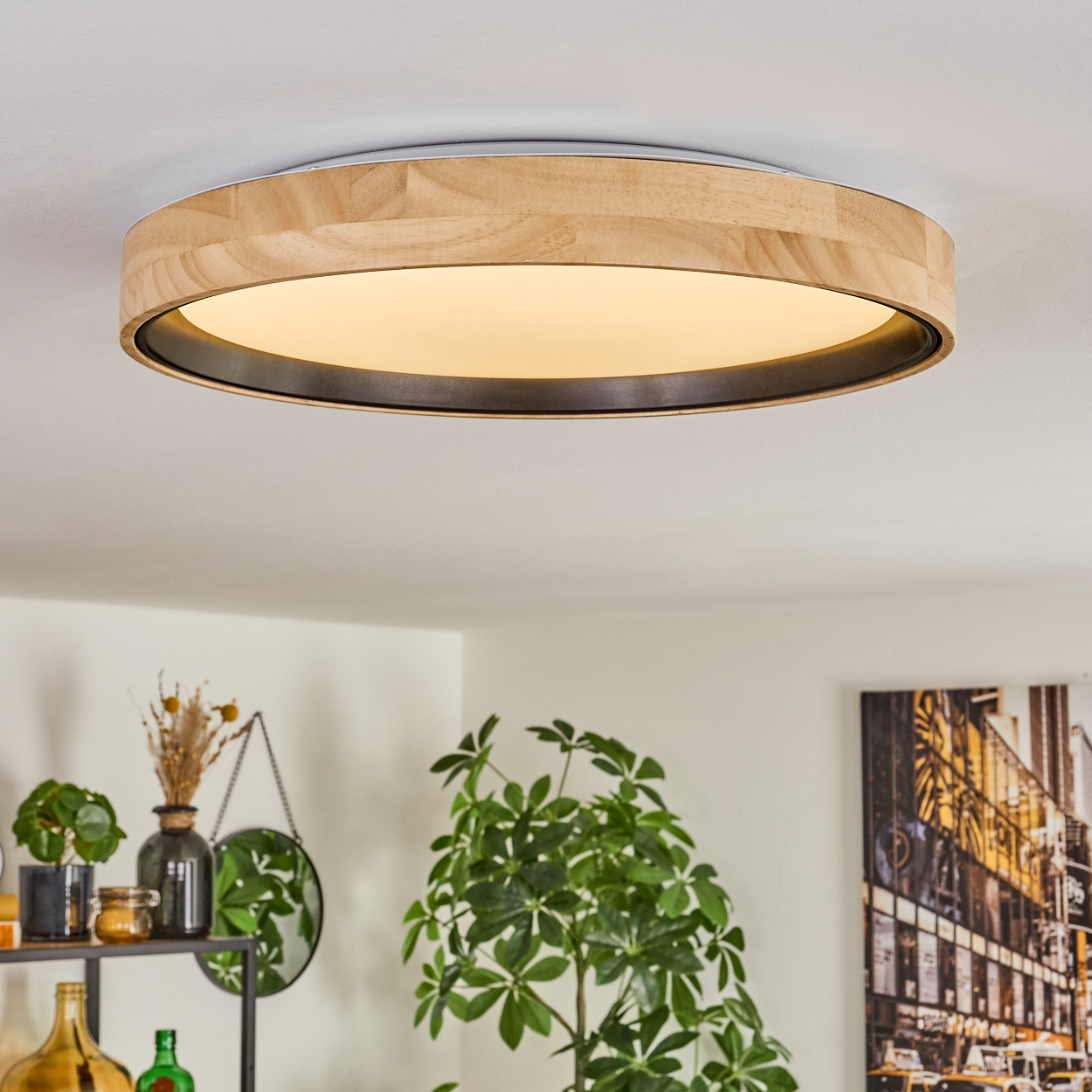 Eine runde Deckenleuchte aus Holz mit hellem Innenlicht. Pflanzen, ein Spiegel und ein Stadtbild schmücken den Raum.