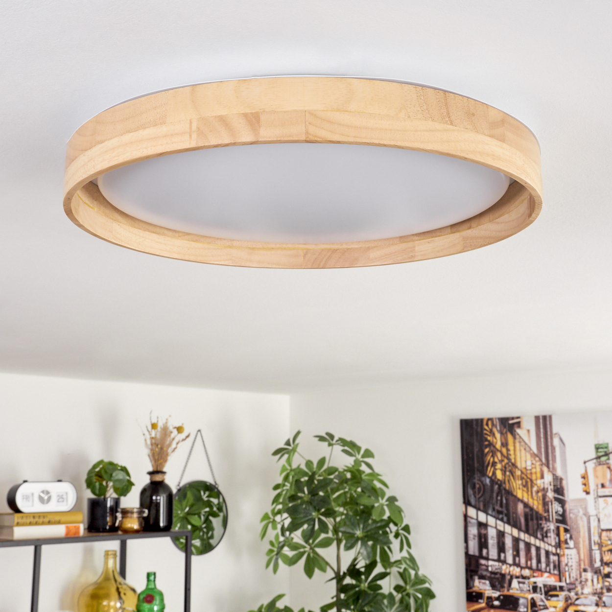 Eine runde Deckenlampe aus Holz. Darunter ein Regal mit Dekoration, eine grüne Pflanze und ein Gemälde einer Stadtszene.