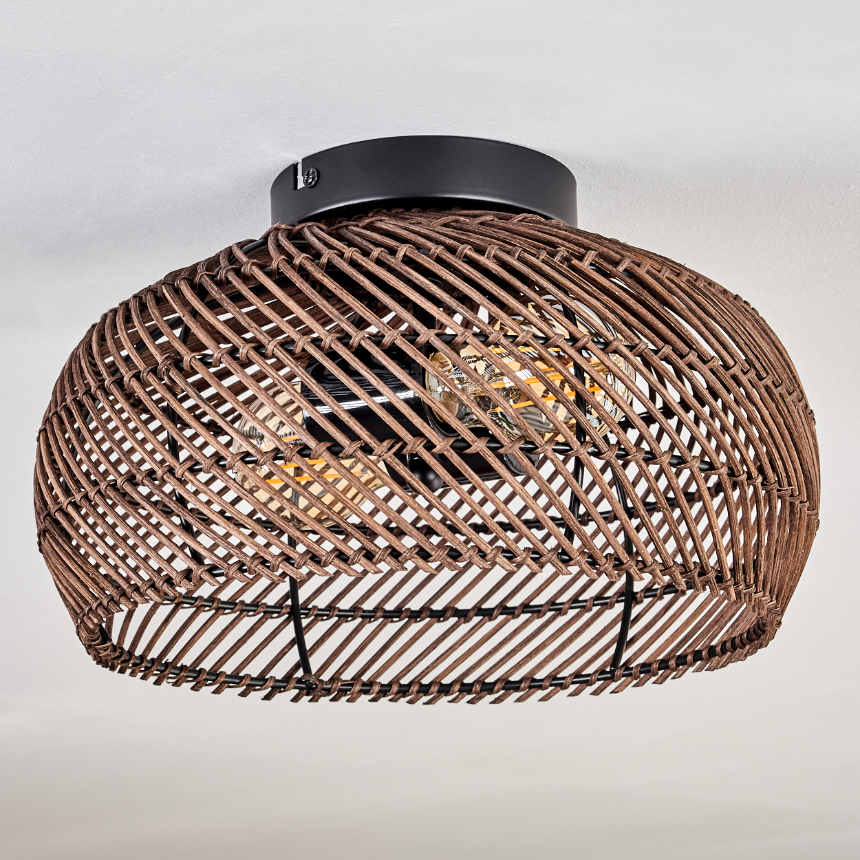 Eine braune Deckenlampe aus gewebtem Rattan mit sichtbaren Glühbirnen, die an einer weißen Decke befestigt ist. Die Leuchte ist kreisförmig.