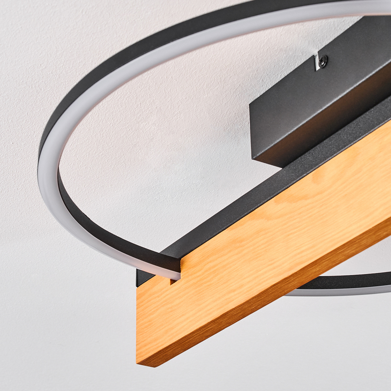 Eine moderne Deckenlampe mit schwarzem Rahmen, Holzbalken und einem weißen, beleuchteten Kreiselement.