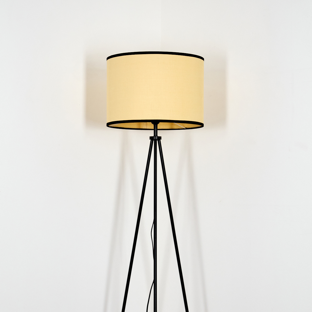 Eine Stehlampe steht vor einer weißen Wand. Sie hat ein schwarzes Stativ und einen beigefarbenen Lampenschirm mit schwarzem Rand.
