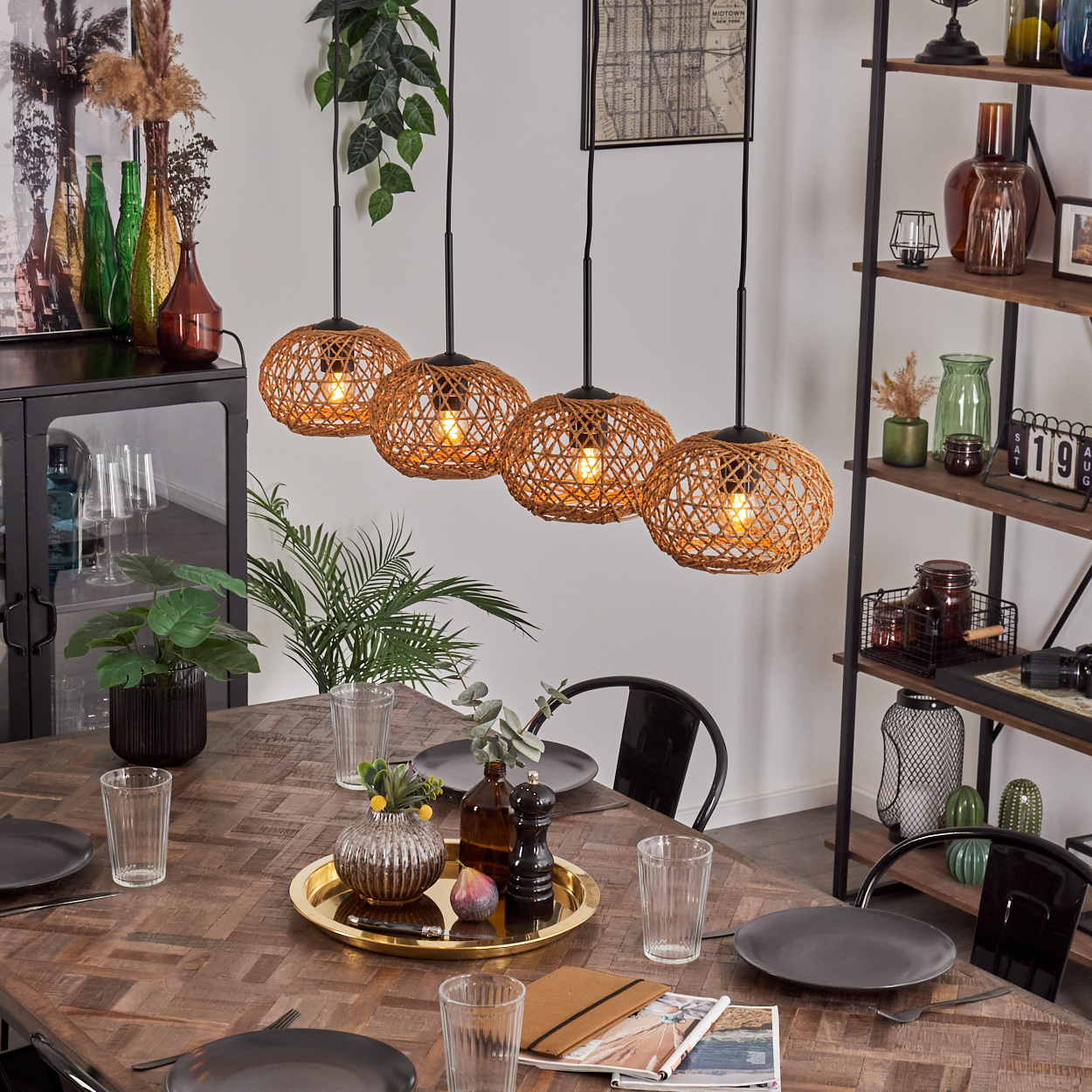 Esszimmer mit Holztisch, gewebten Pendelleuchten. Tischdekoration mit Tellern, Gläsern und einer Dekoschale. Regale mit Objekten.