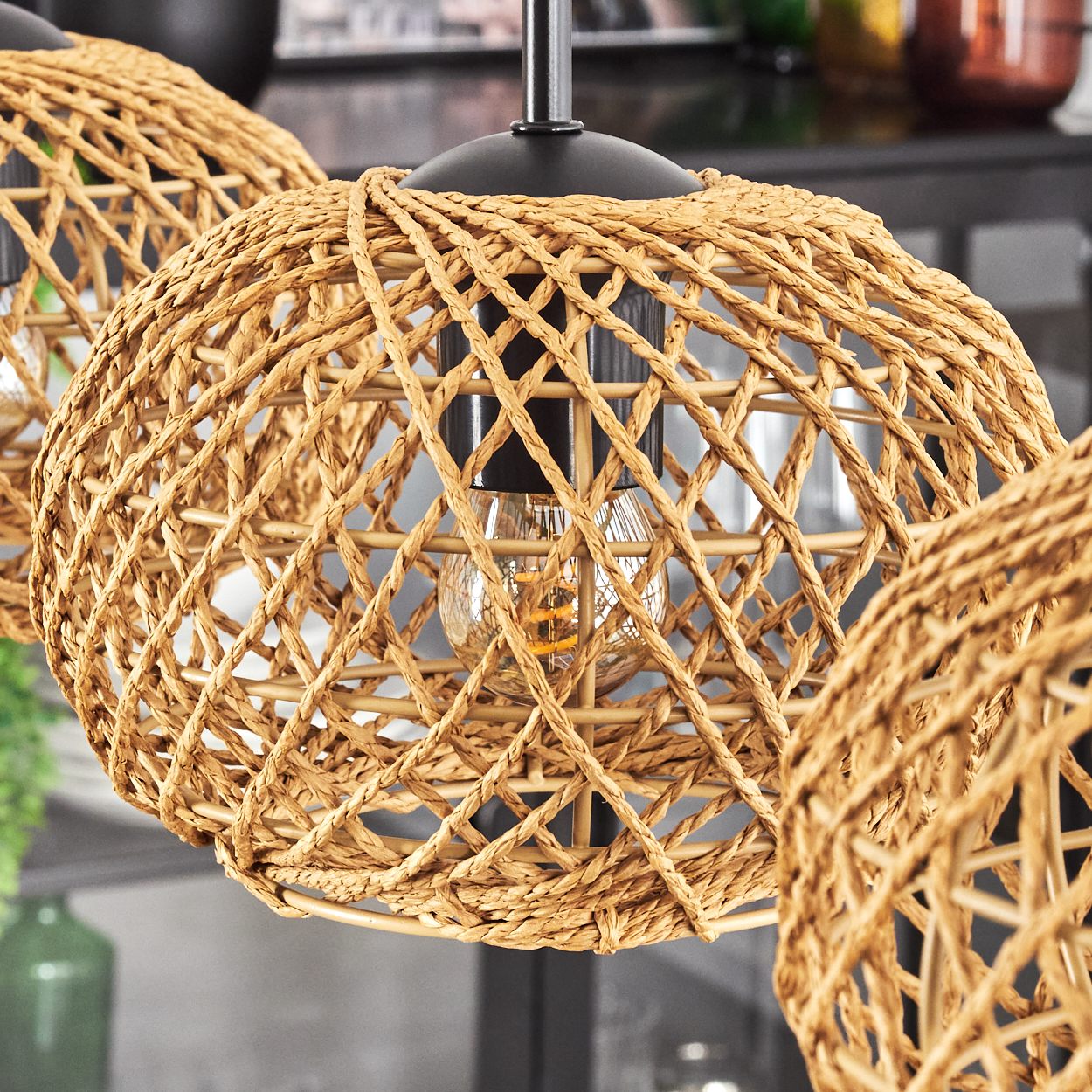 Nahaufnahme von geflochtenen Pendelleuchten aus Rattan mit sichtbaren Glühbirnen. Der Hintergrund zeigt Einblicke in einen Raum.