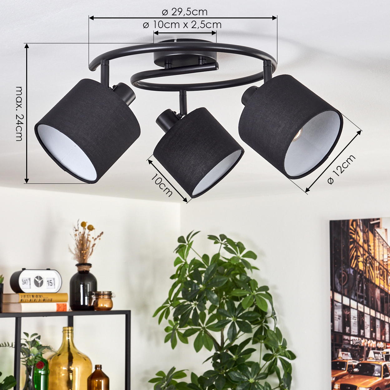Eine schwarze Deckenlampe mit drei verstellbaren Strahlern. Abmessungen sind angegeben. Innenraum mit Pflanzen, Büchern und Kunstwerken.
