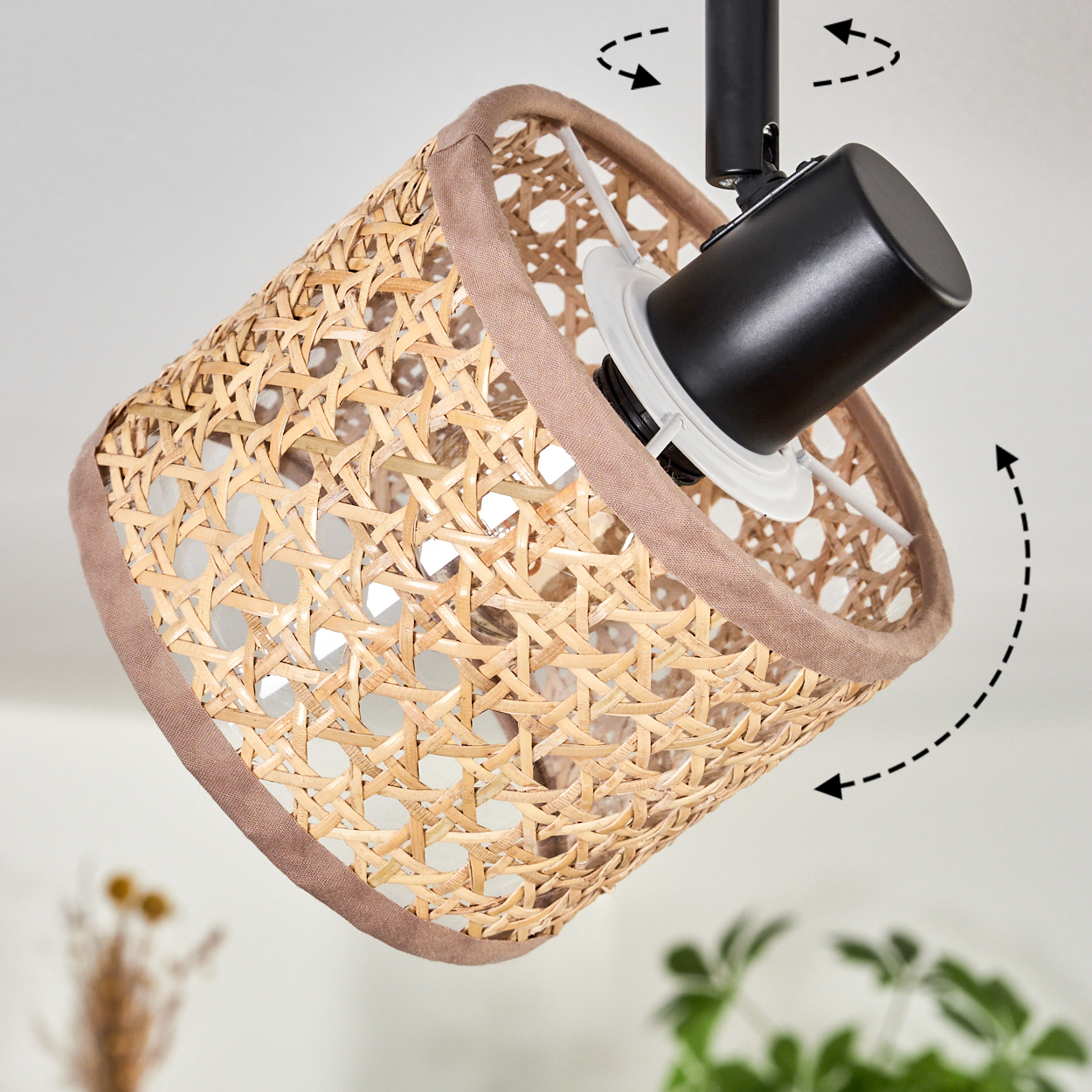 Ein gewebter Lampenschirm, beige und braun, hängt an einer schwarzen Halterung. Pfeile zeigen die verstellbare Richtung an.