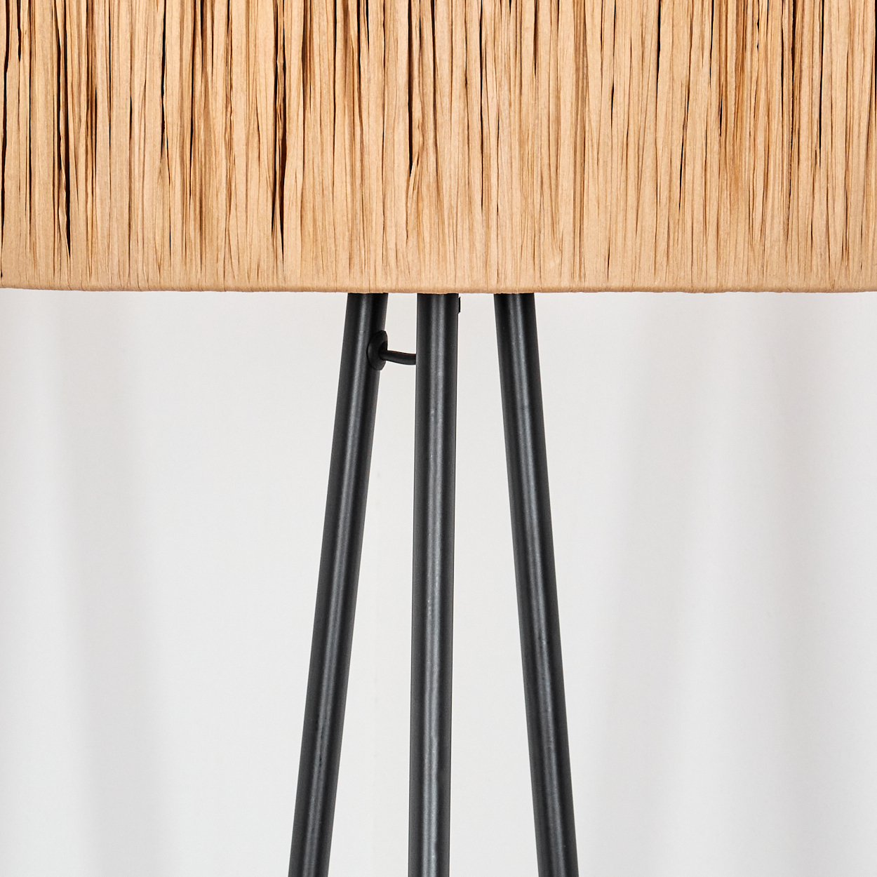 Nahaufnahme einer Lampe mit beigem, strukturiertem Lampenschirm und schwarzen Stativbeinen vor weißem Hintergrund.