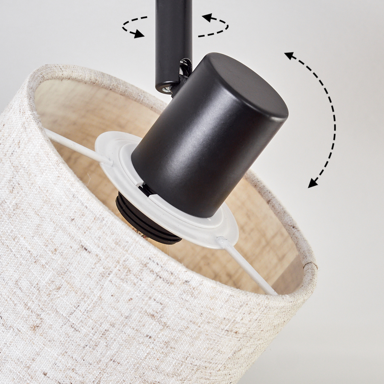 Nahaufnahme einer Lampe mit schwarzem, verstellbarem Kopf. Der Lampenschirm ist beige. Pfeile zeigen die Bewegung der Lampe. Weißer Hintergrund.