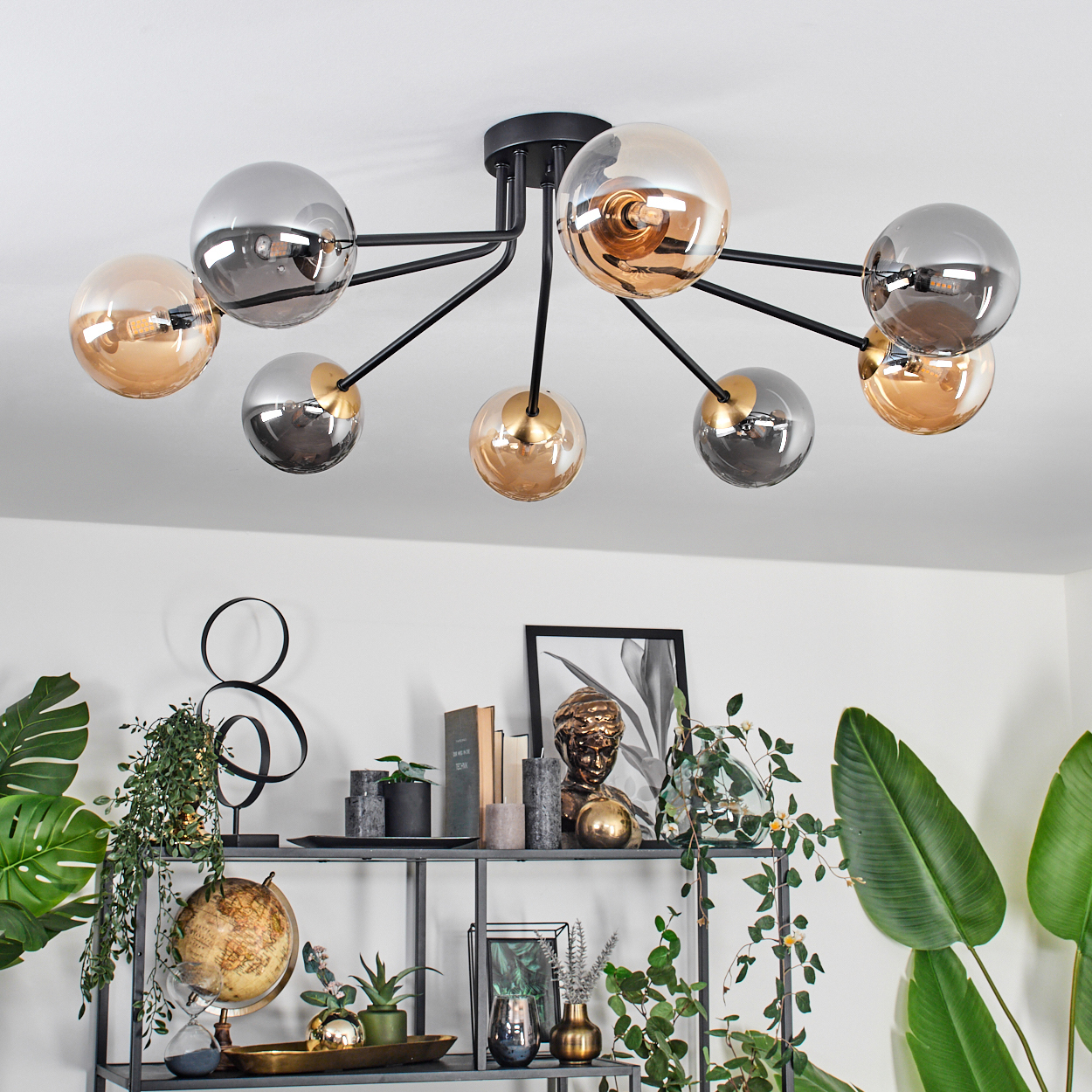 Eine moderne Deckenleuchte mit Glaskugeln und ein Regal mit dekorativen Gegenständen und Pflanzen. Die Decke ist weiß.