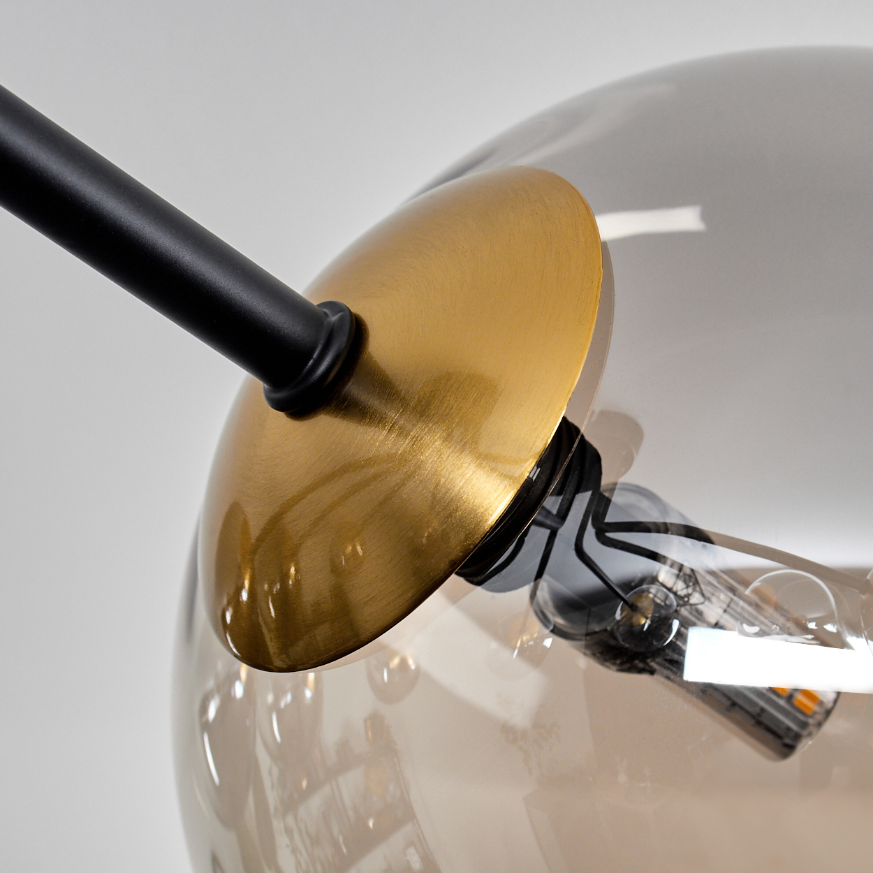 Nahaufnahme einer modernen Lampe. Sie hat eine goldfarbene Scheibe, einen schwarzen Arm und eine transparente Glühbirne.