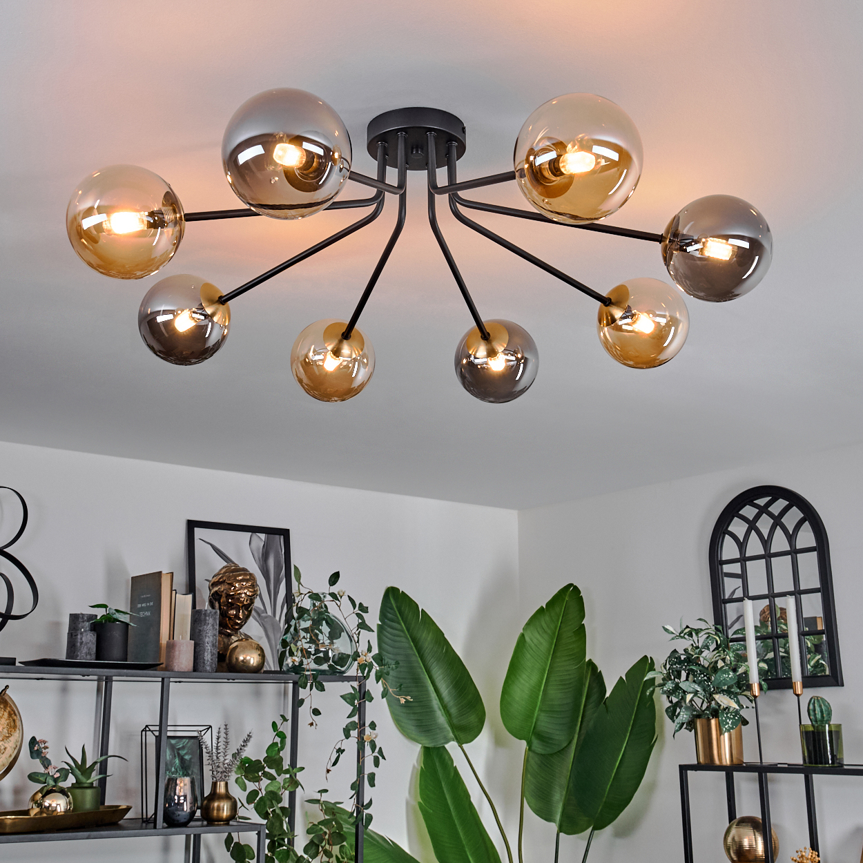 Deckenlampe mit mehreren Glaskugeln. Der Raum hat Pflanzen, Regale mit Dekorationen und einen bogenförmigen Spiegel.