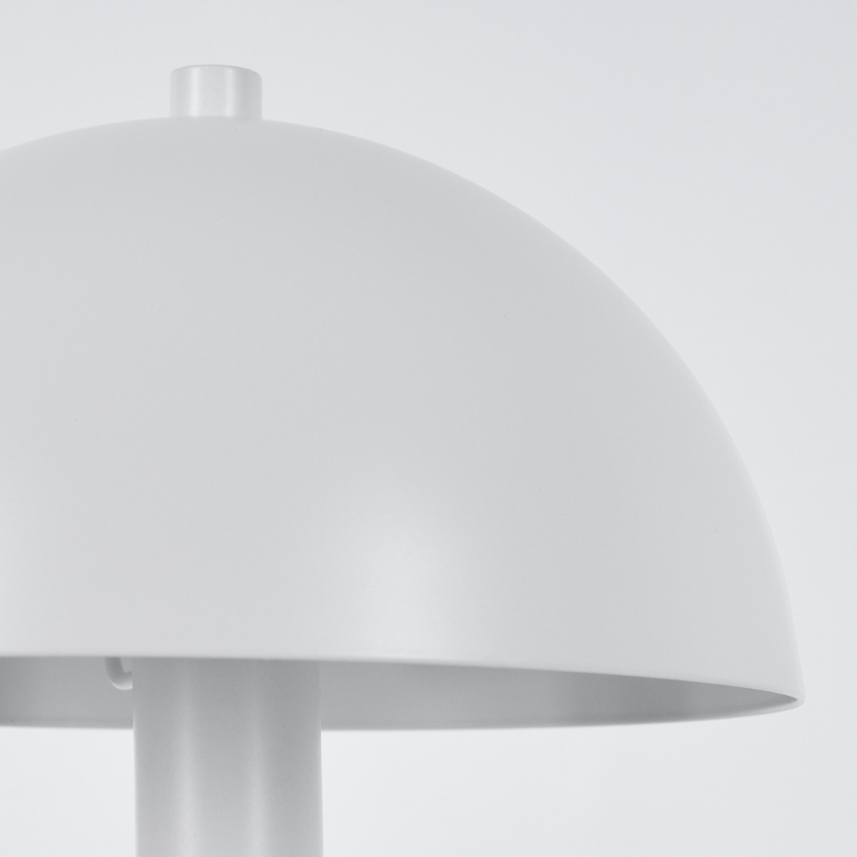 Nahaufnahme einer weißen Lampe mit rundem Schirm. Die Lampe hat einen Stiel und einen kleinen Aufsatz. Der Hintergrund ist weiß.