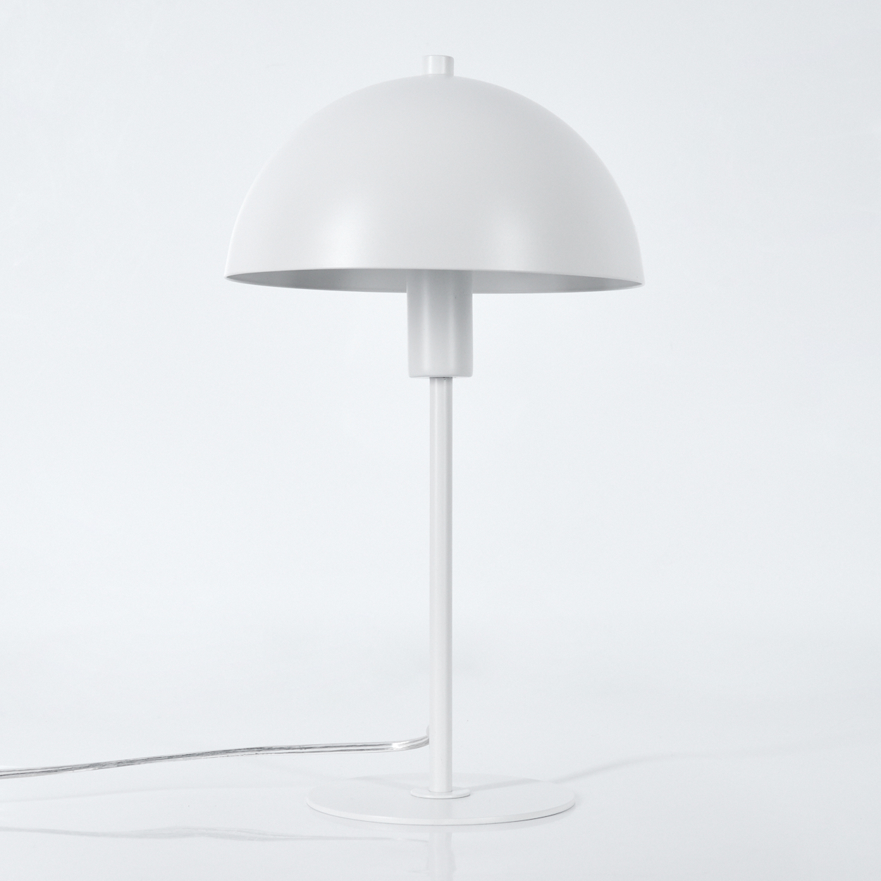 Eine weiße Tischlampe mit gewölbtem Schirm, dünnem Stiel und rundem Fuß. Ein Netzkabel erstreckt sich nach links.
